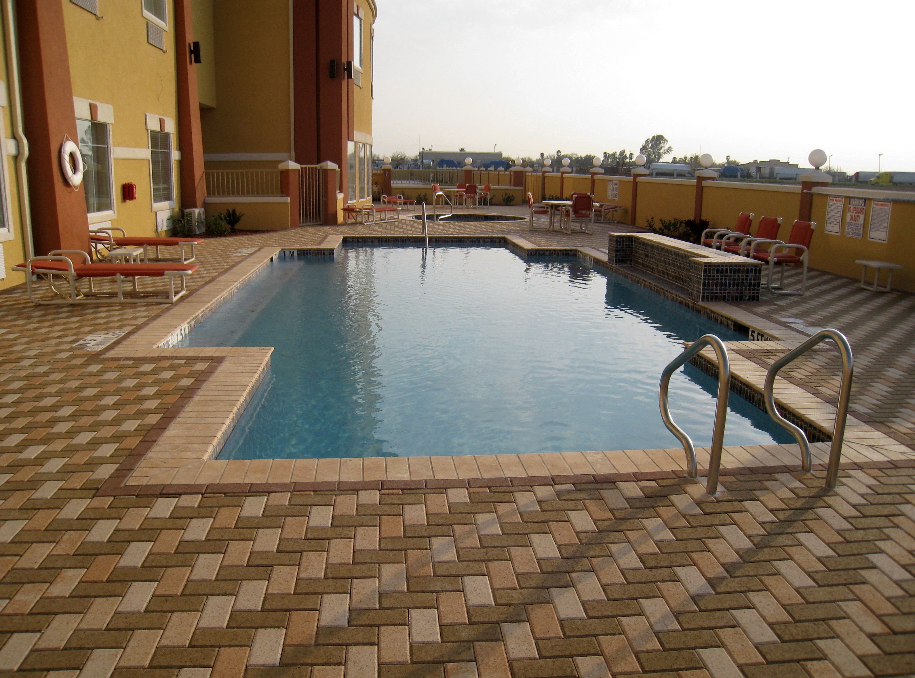 A swimming pool with a brick deck, lounge chairs, and a lifebuoy.