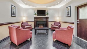 A lobby with a fireplace, four armchairs, a coffee table, and a television mounted above the fireplace. - Super 8 by Wyndham Hidalgo/McAllen Area (Hidalgo)
