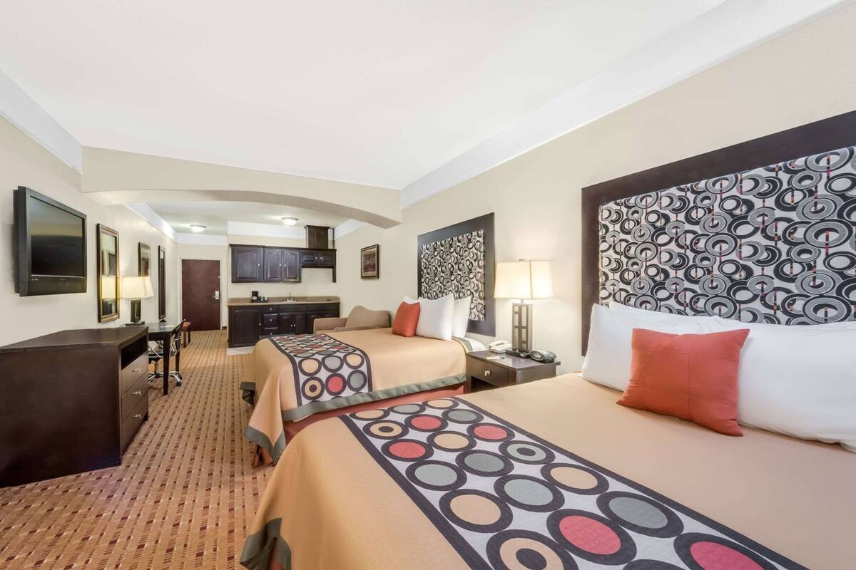 Een hotelkamer met twee bedden, een bureau, een stoel, een kleine kitchenette en een televisie.