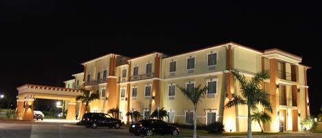 A multi-story hotel with a central entrance, several balconies, and palm trees in the landscaping.