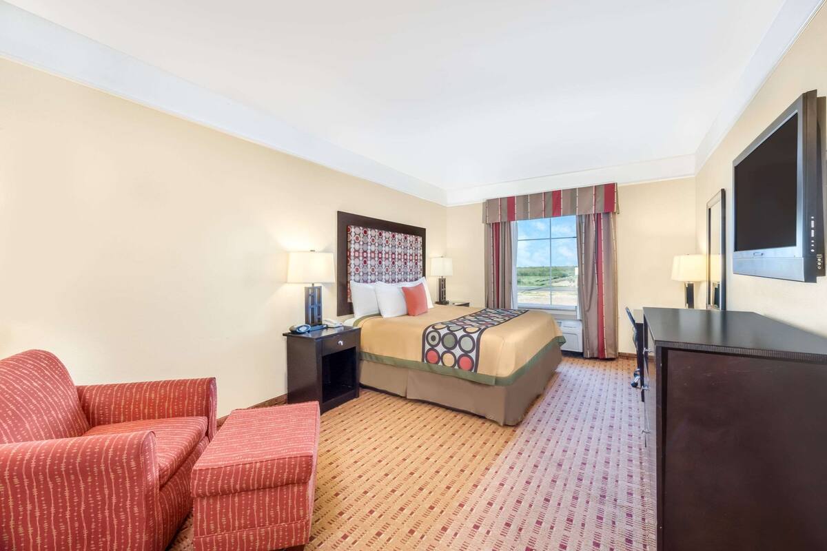 Een hotelkamer met een bed, een bureau, een stoel, een televisie en een raam met gordijnen.
