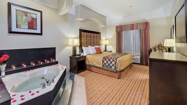 A hotel room with a large bathtub, a bed with a patterned headboard, two bedside lamps, and a desk with a chair. - Super 8 by Wyndham Hidalgo/McAllen Area (Hidalgo)