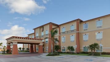 A multi-story hotel with a covered entrance, palm trees, and a clear sky.