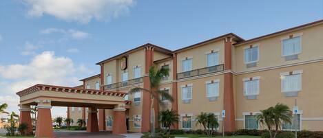 A multi-story hotel with a covered entrance, palm trees, and a clear sky.