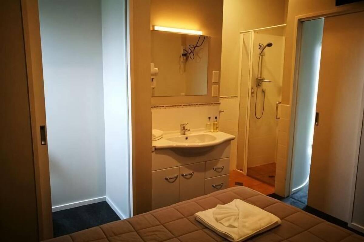 Une chambre d’hôtel comprenant un lit, une salle de bain avec un lavabo et une douche, et une porte donnant sur une autre pièce.