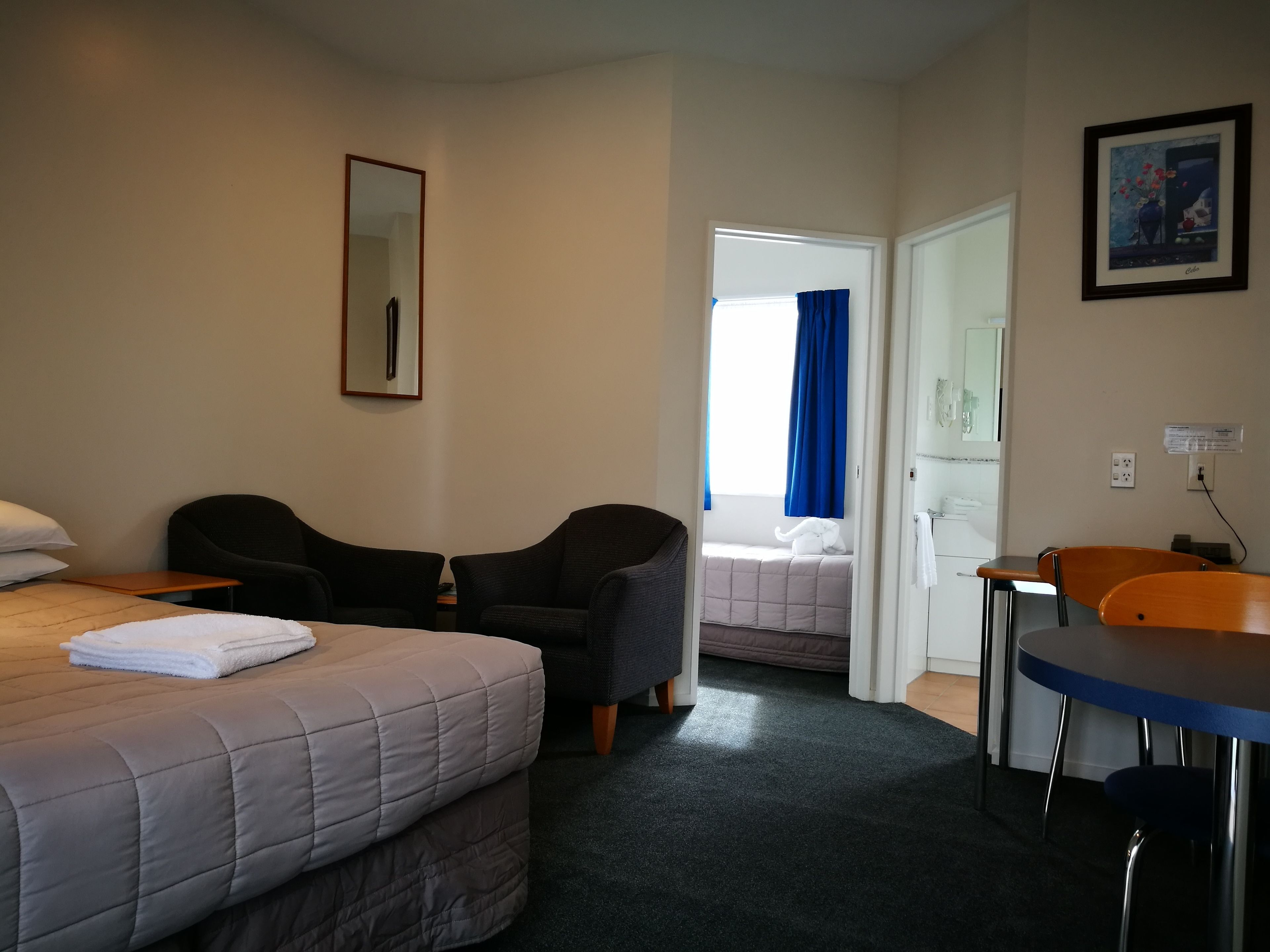 A hotel room with a bed, two armchairs, a desk, and a window with blue curtains.