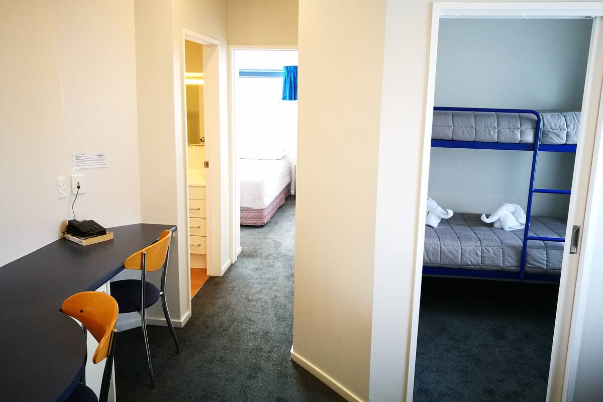 Une chambre avec des lits superposés, un bureau avec une chaise et un petit placard.