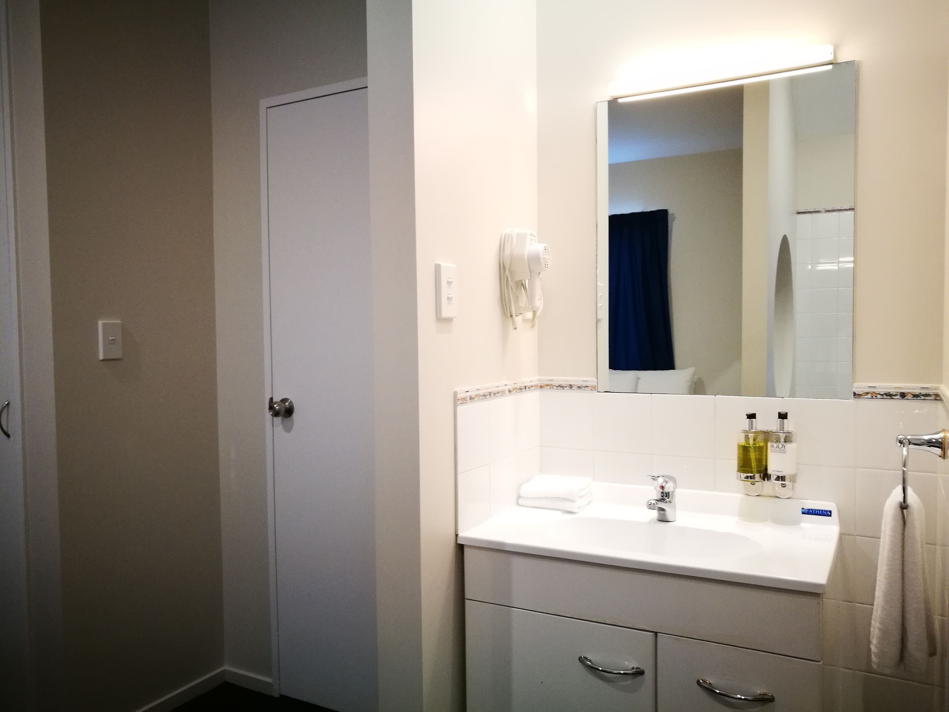 Un baño con un lavamanos blanco, un espejo, una toalla colgada en la pared y una puerta.