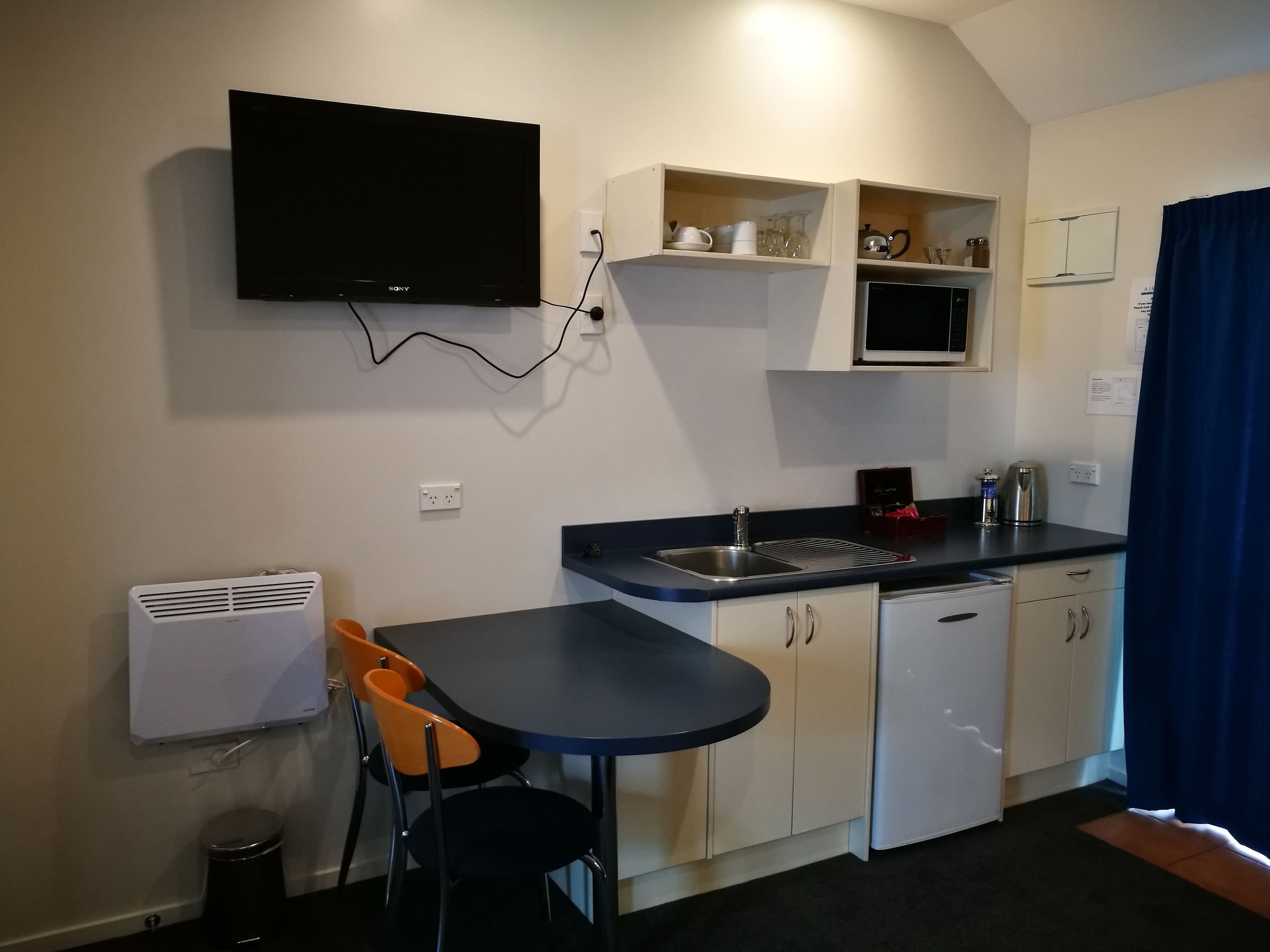 A compact kitchen with a built-in TV, a sink, and a small dining area with two chairs.