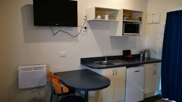 A compact kitchen with a built-in TV, a sink, and a small dining area with two chairs.