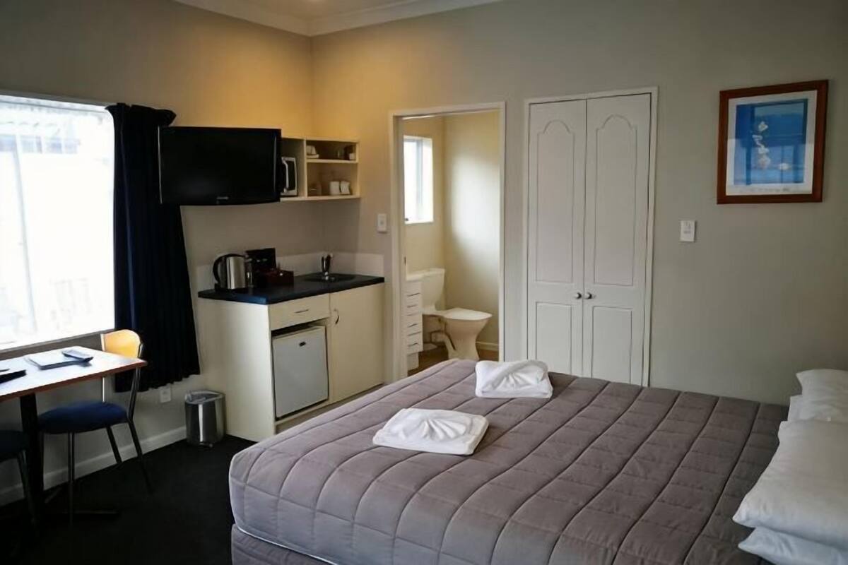 Une chambre d’hôtel équipée d’un lit, d’un bureau, d’une kitchenette, d’une télévision et d’une porte.