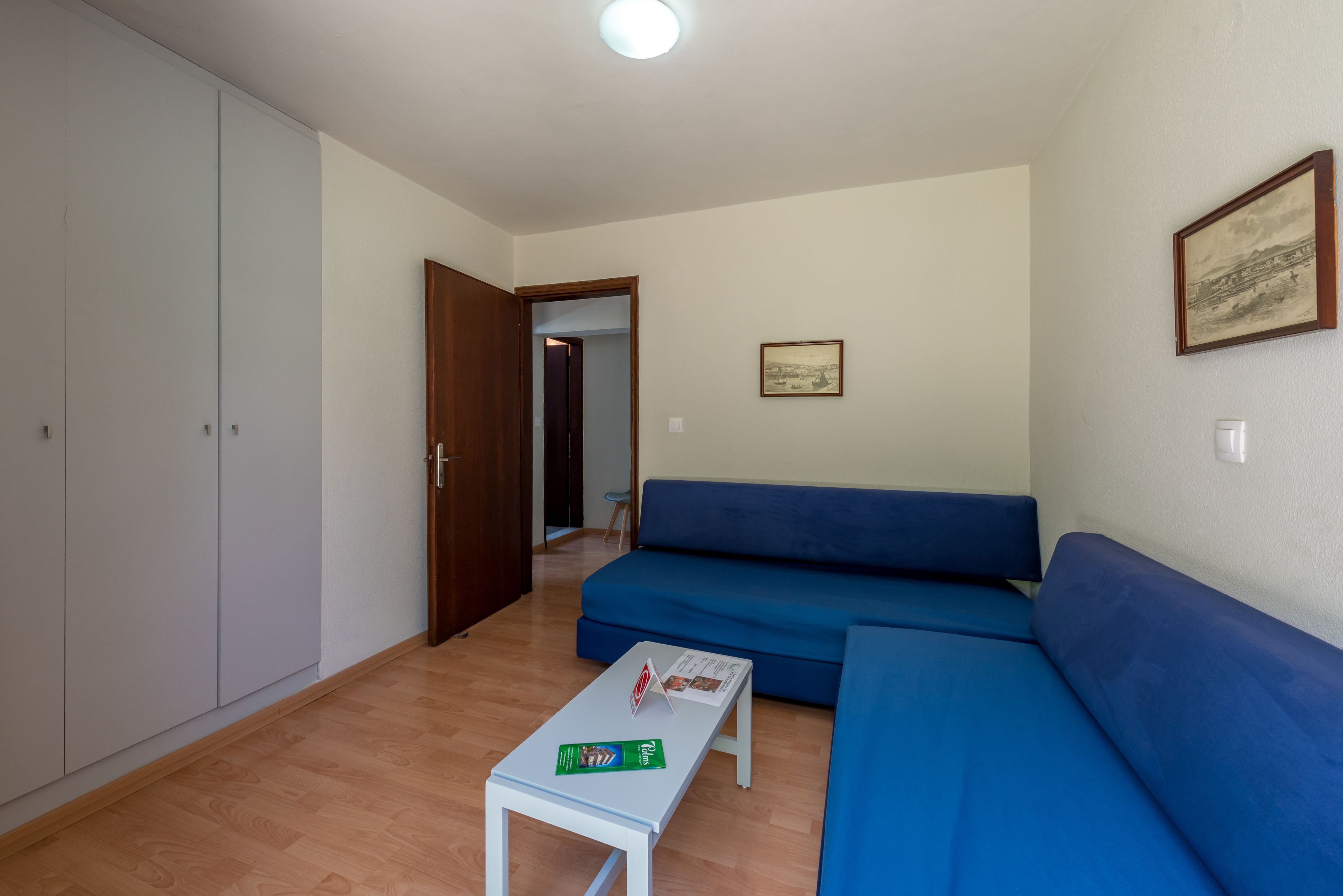 Ein Zimmer mit einem blauen Sofa, einem weißen Tisch mit Zeitschriften, einem Holzschrank und einem gerahmten Bild an der Wand.