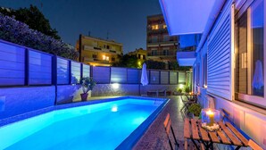 A swimming pool with tiled edges, a wooden deck, and a small table with a candle. - 7 Palms Hotel Apartments (Rhodes)