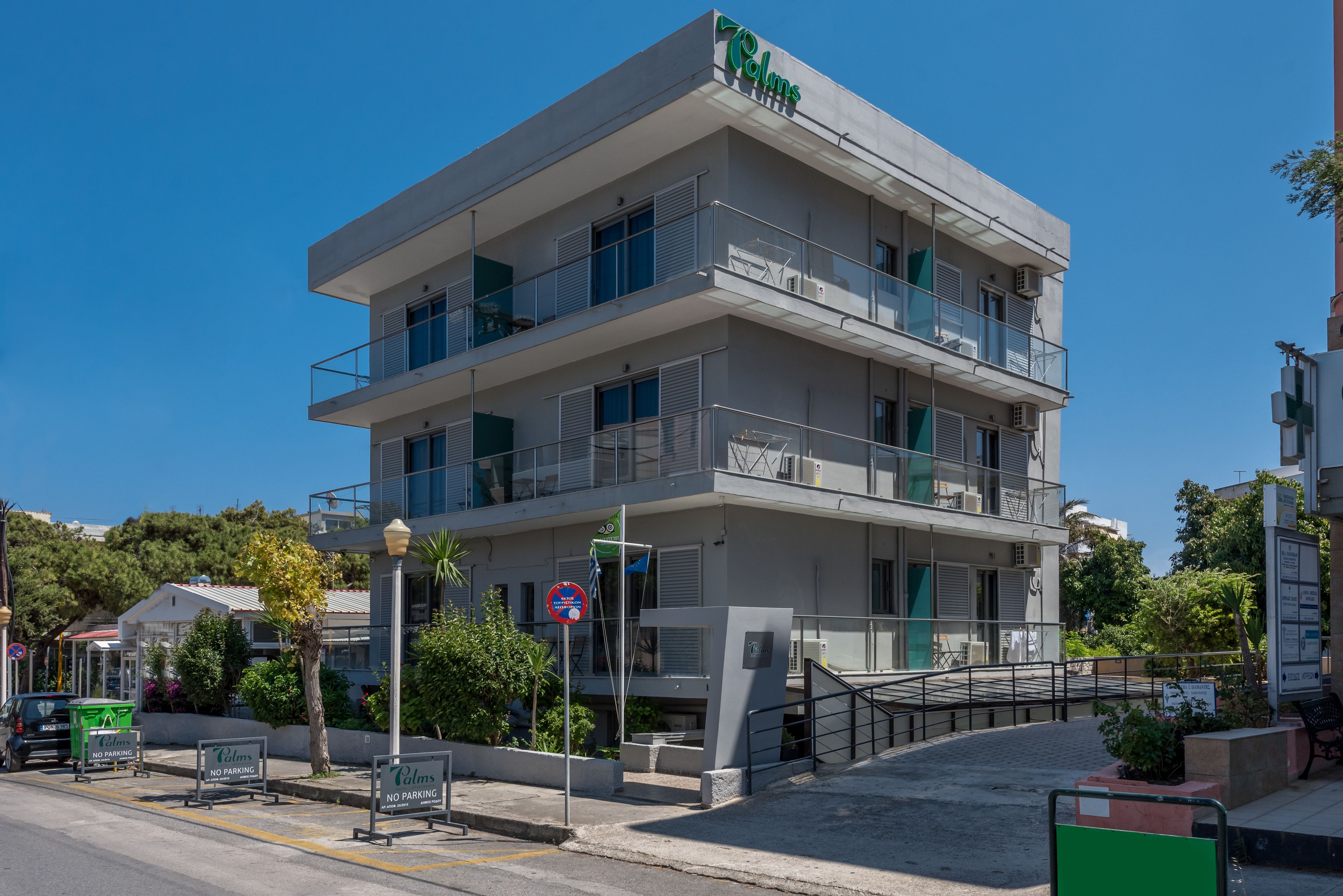 A multi-story hotel with balconies, a "No Parking" sign, and a "No Parking" sign on the street.