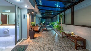 A reception area with a glass wall, a reception desk, and a seating area with a bench and a table. - 7 Palms Hotel Apartments (Rhodes)