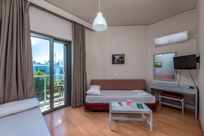 Quarto de hotel moderno com uma grande porta de vidro deslizante para uma varanda, uma cama, uma escrivaninha e uma televisão.