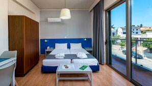 A modern hotel room with a large bed, a desk, and a view of the street through a large window. - 7 Palms Hotel Apartments (Rhodes)