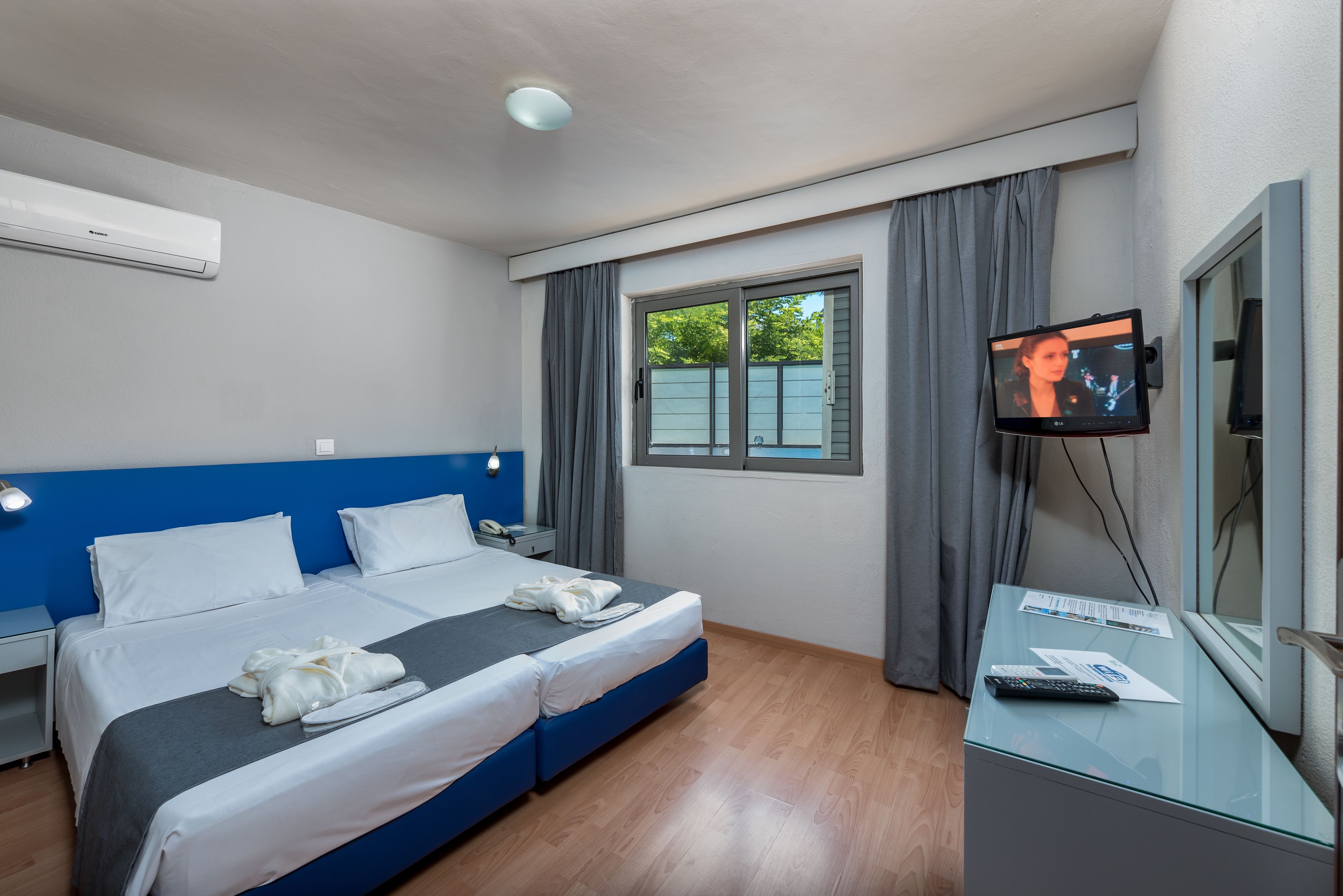 A hotel room with a bed, a desk with a TV, and a window with curtains.