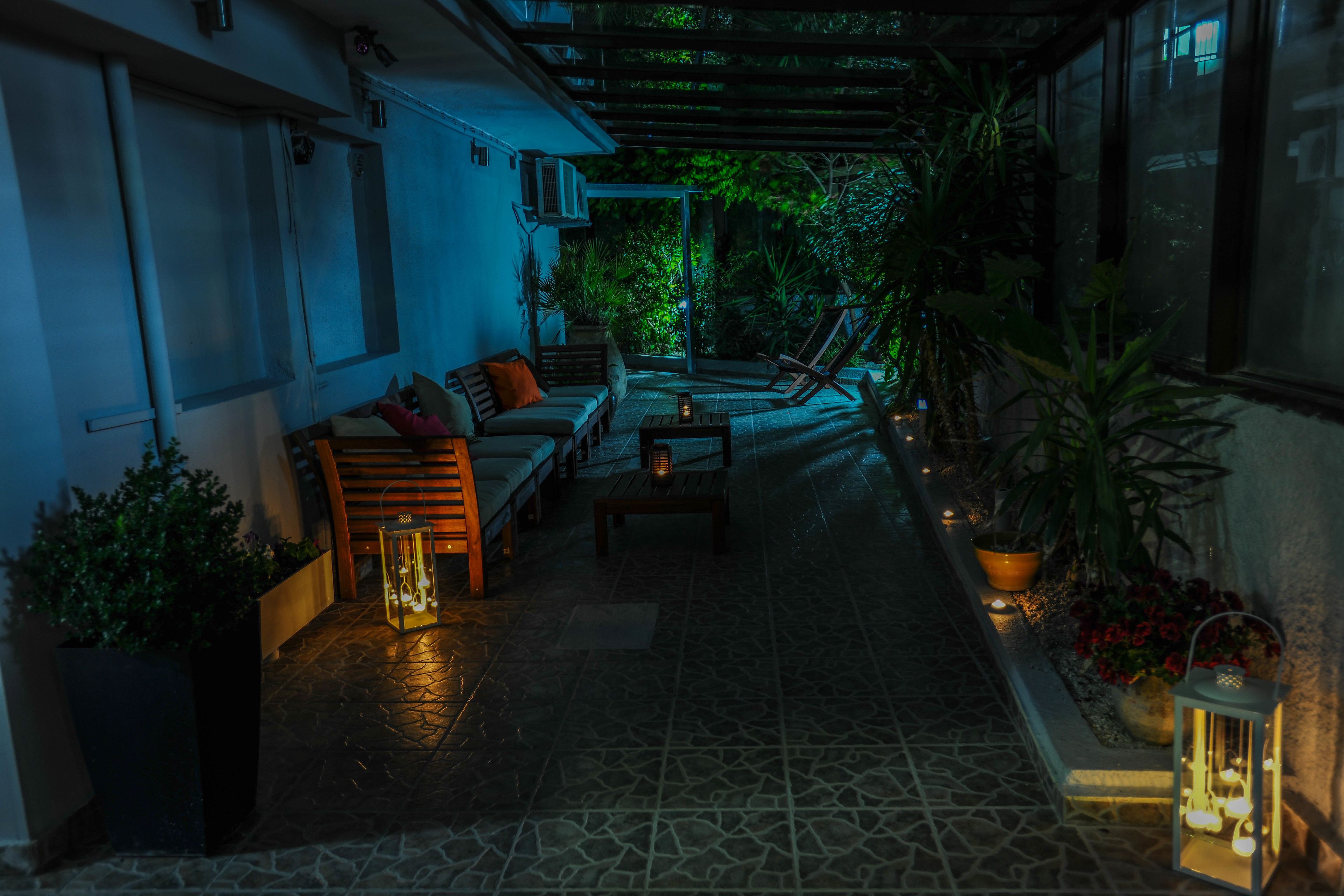 A covered outdoor patio with a sofa, chairs, and a table, surrounded by potted plants and a lantern.