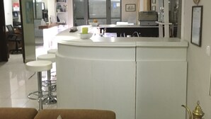 A modern kitchen with white cabinetry, a central island with stools, and a dining area with a white table and chairs. - 7 Palms Hotel Apartments (Rhodes)