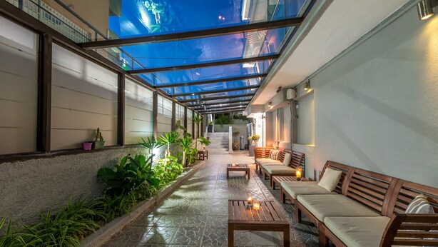 A covered outdoor area with stone flooring, wooden benches, and potted plants. - 7 Palms Hotel Apartments (Rhodes)