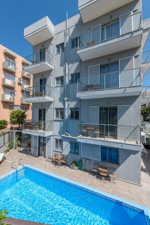 Um edifício moderno de vários andares com piscina, área de estar externa e varandas.