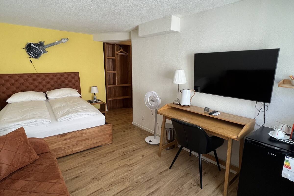 A hotel room with a bed, a desk, a TV, a fan, and a wardrobe.