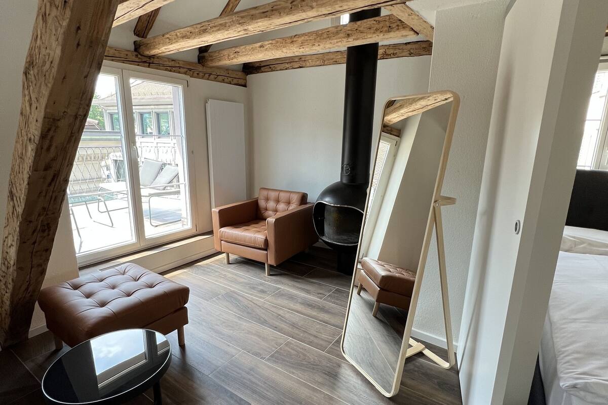 A cozy room with a sloped ceiling, wooden beams, a large mirror, a sofa, and a small table.