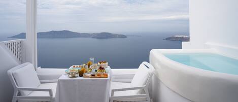 A balcony with a white table set for breakfast, a white chair, and a hot tub.