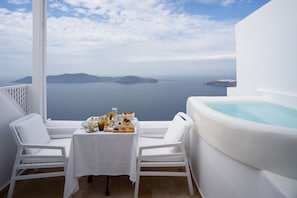 A balcony with a white table set for breakfast, a white chair, and a hot tub.