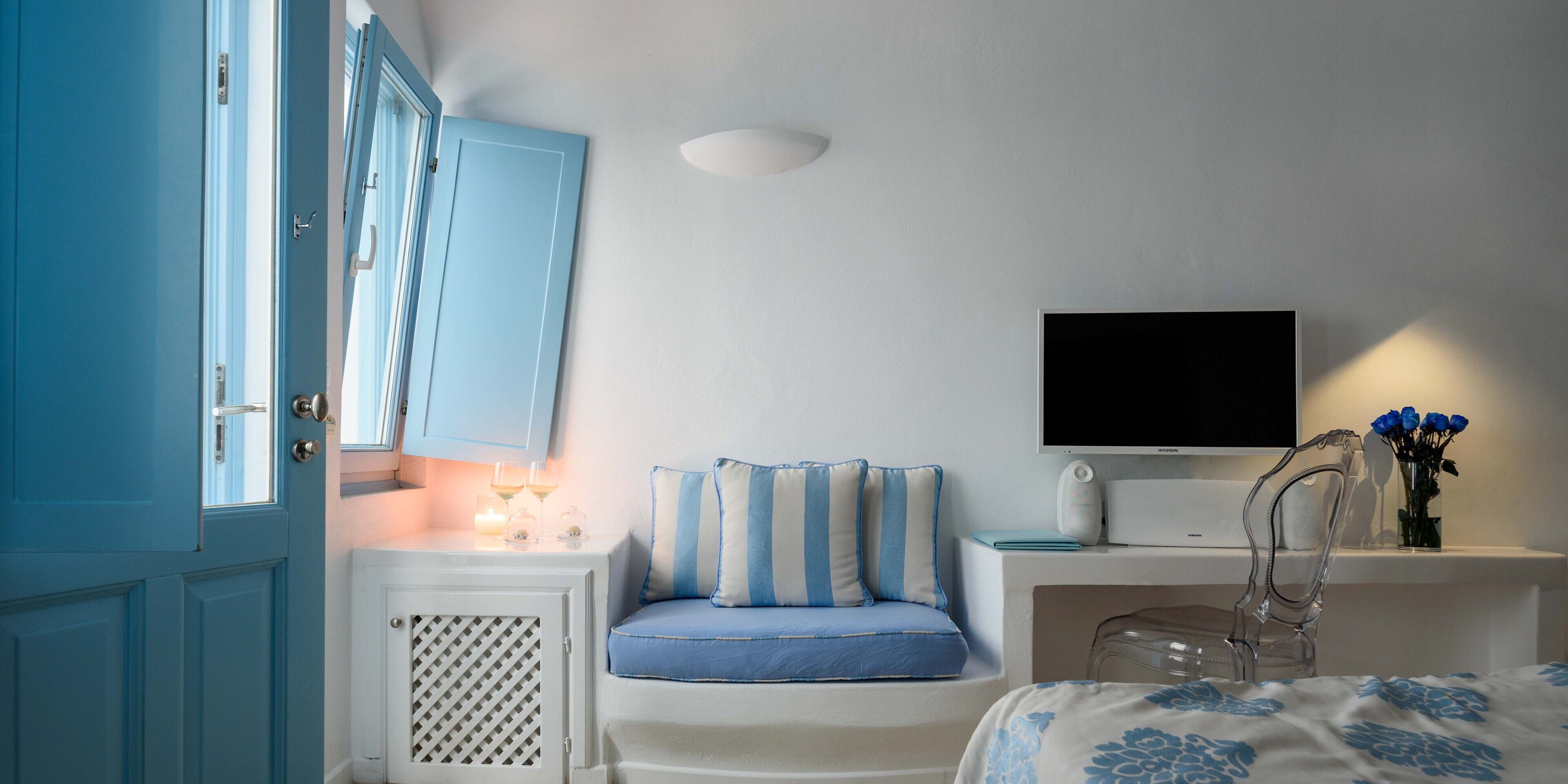 A bedroom with a bed, a TV, a chair, a desk, and a window with curtains.