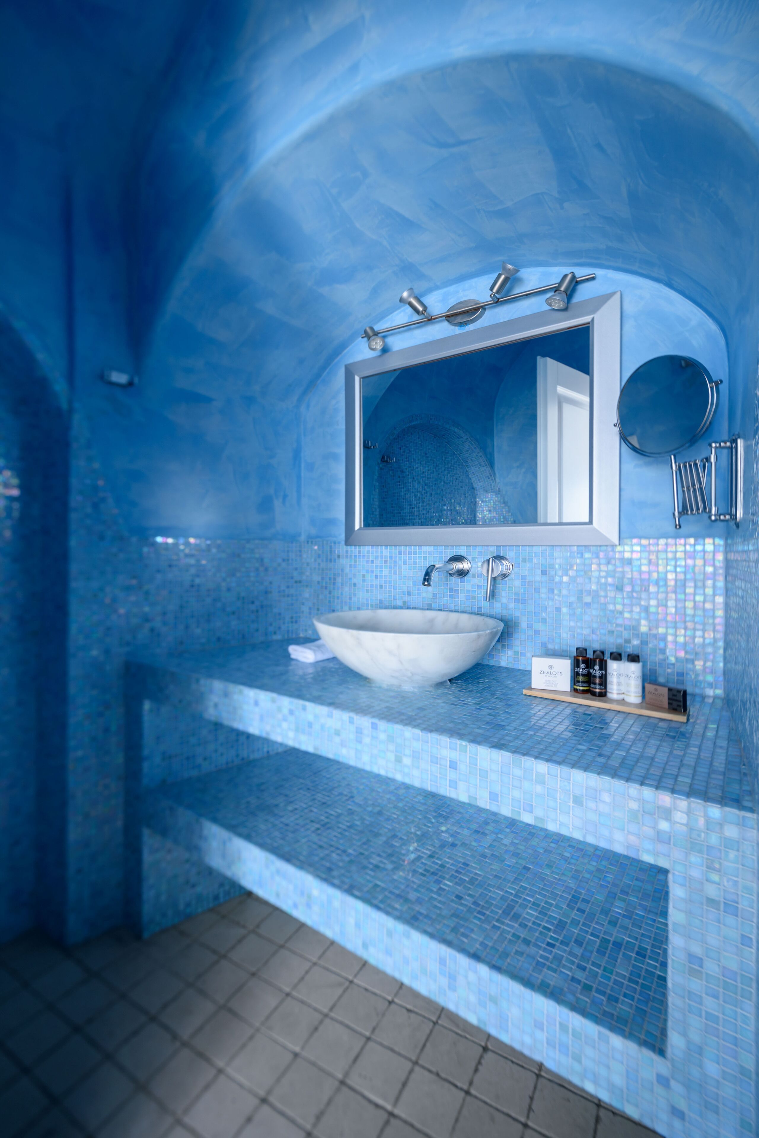 A bathroom with a large white sink, a mirror, and a blue-tiled shower area.