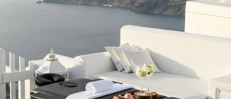 A sun lounger with a towel and two drinks, overlooking a coastal view with a cliff and the sea.