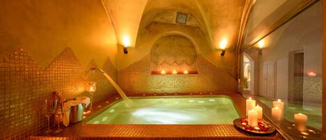 A luxurious spa with a large bathtub, tiled walls, and candles.