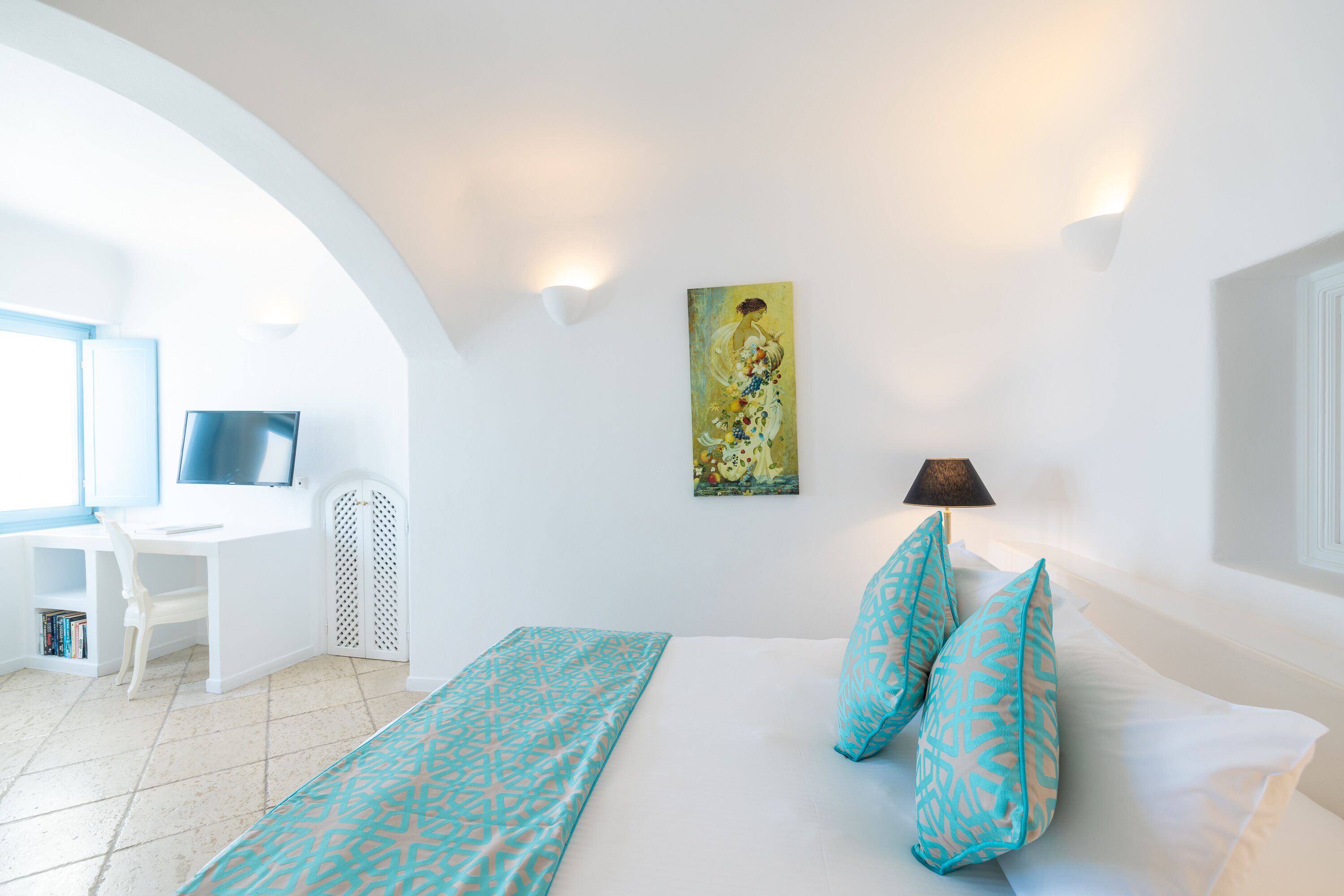 A hotel room with a bed, a desk, a chair, a TV, and a painting on the wall.