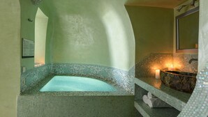Un área de spa con una bañera con mosaicos, un lavabo de mármol y un espejo montado en la pared.