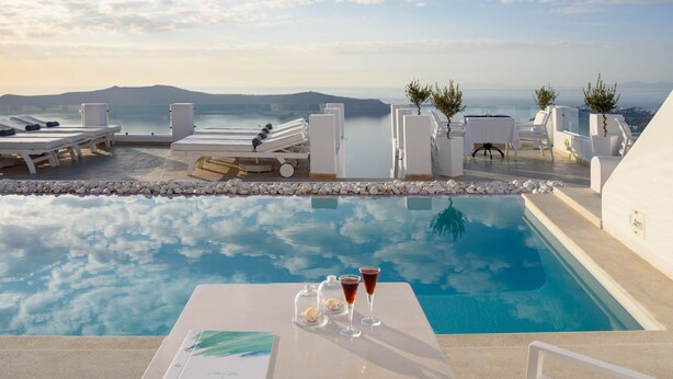 Zona junto a la piscina con sillones, una mesa con bebidas y vistas al mar y las montañas.
