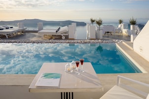 A poolside area with lounge chairs, a table with drinks, and a view of the sea and mountains.