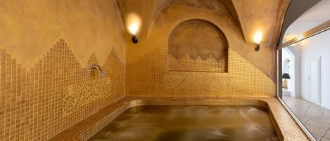 Un jacuzzi grande y rectangular con paredes y techo de mosaicos, rodeado por un piso de baldosas.