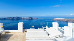 Un salón junto al mar con sillones blancos y una vista despejada del océano y una isla rocosa en la distancia.
