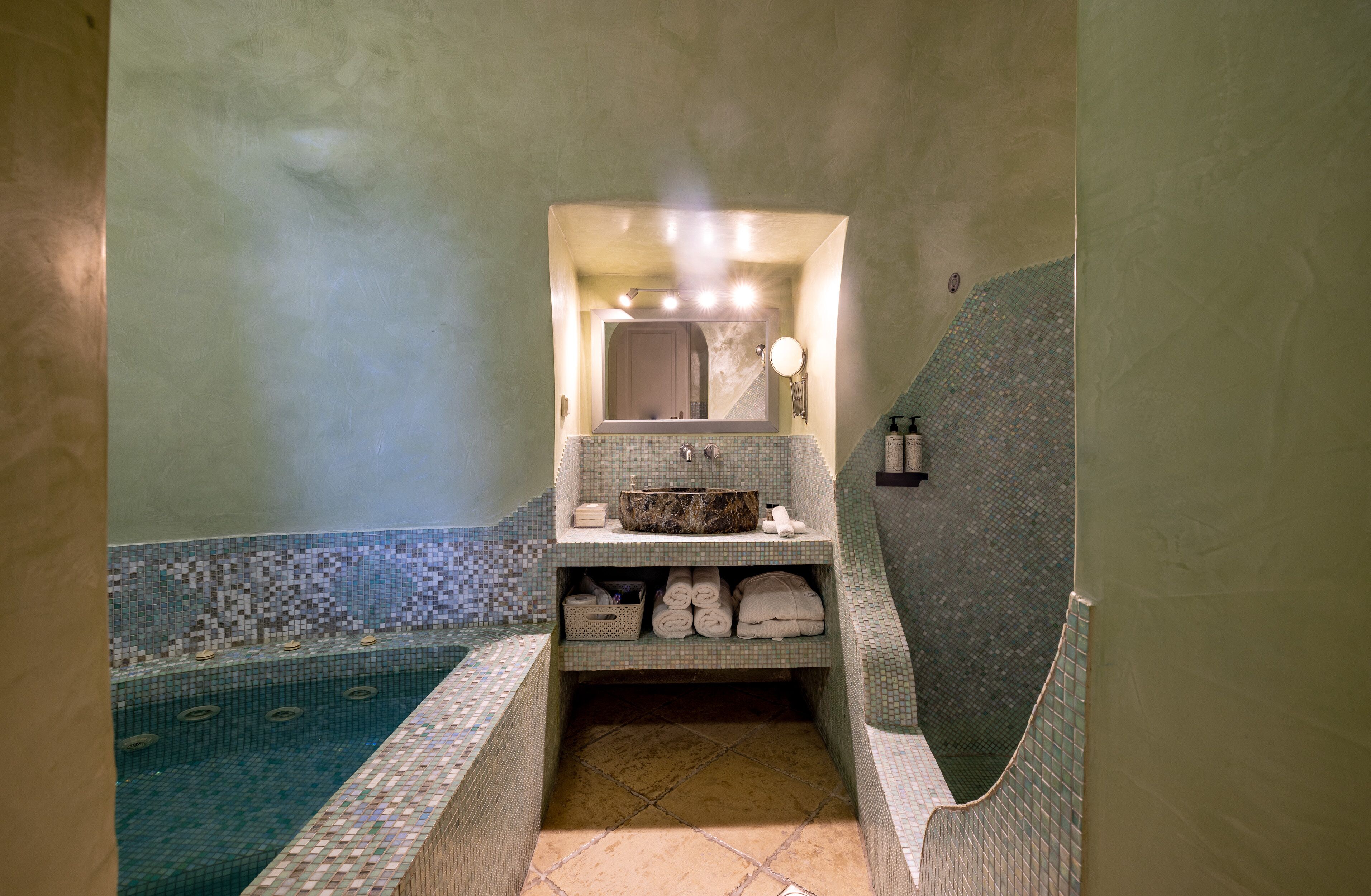 Un baño con piso de baldosas, un lavamanos con espejo y zona de ducha.
