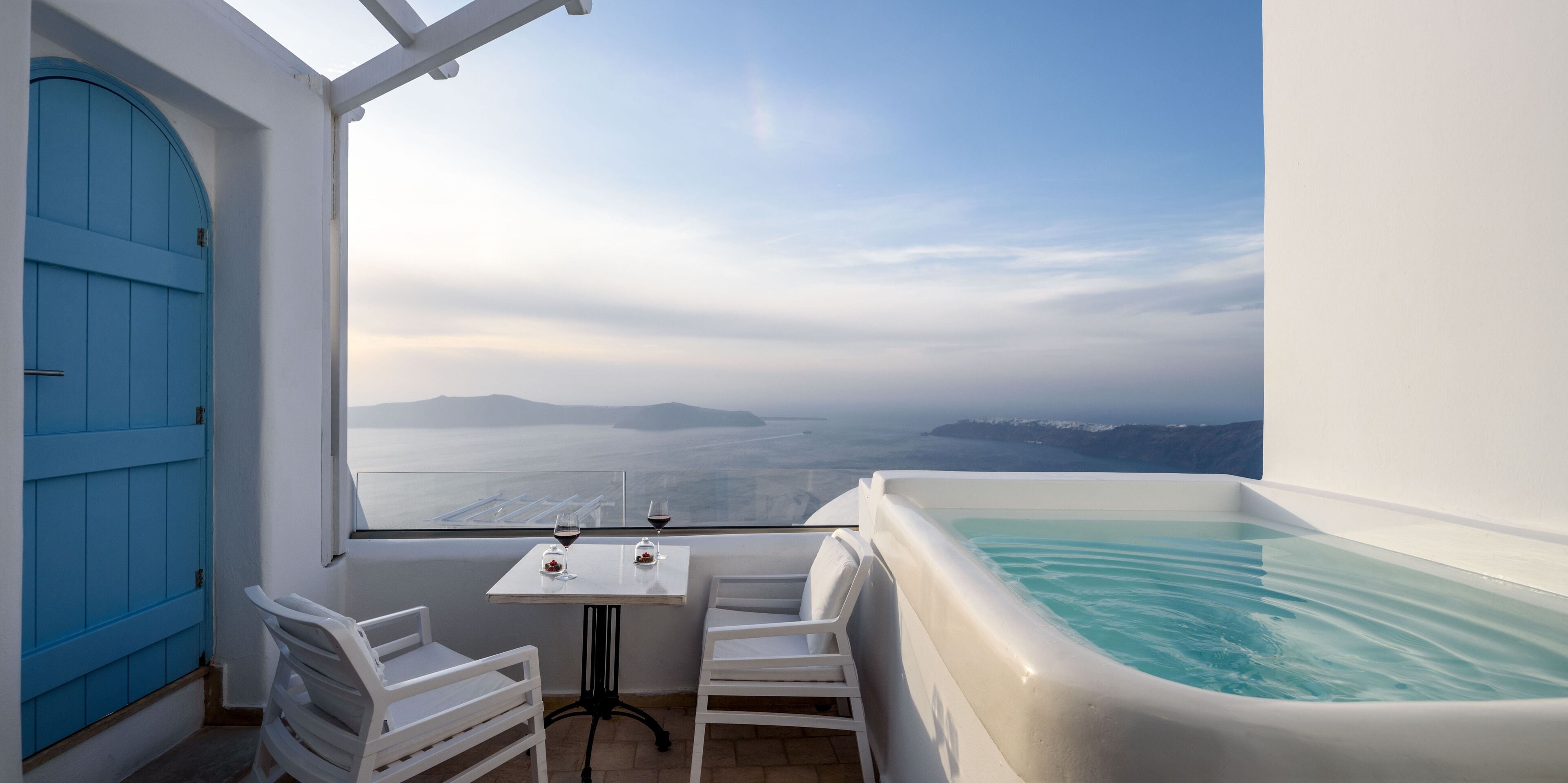 A balcony with a white table, two white chairs, and a large bathtub.