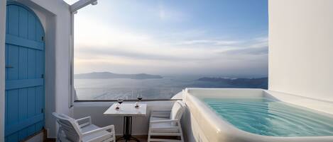 A balcony with a white table, two white chairs, and a large bathtub.