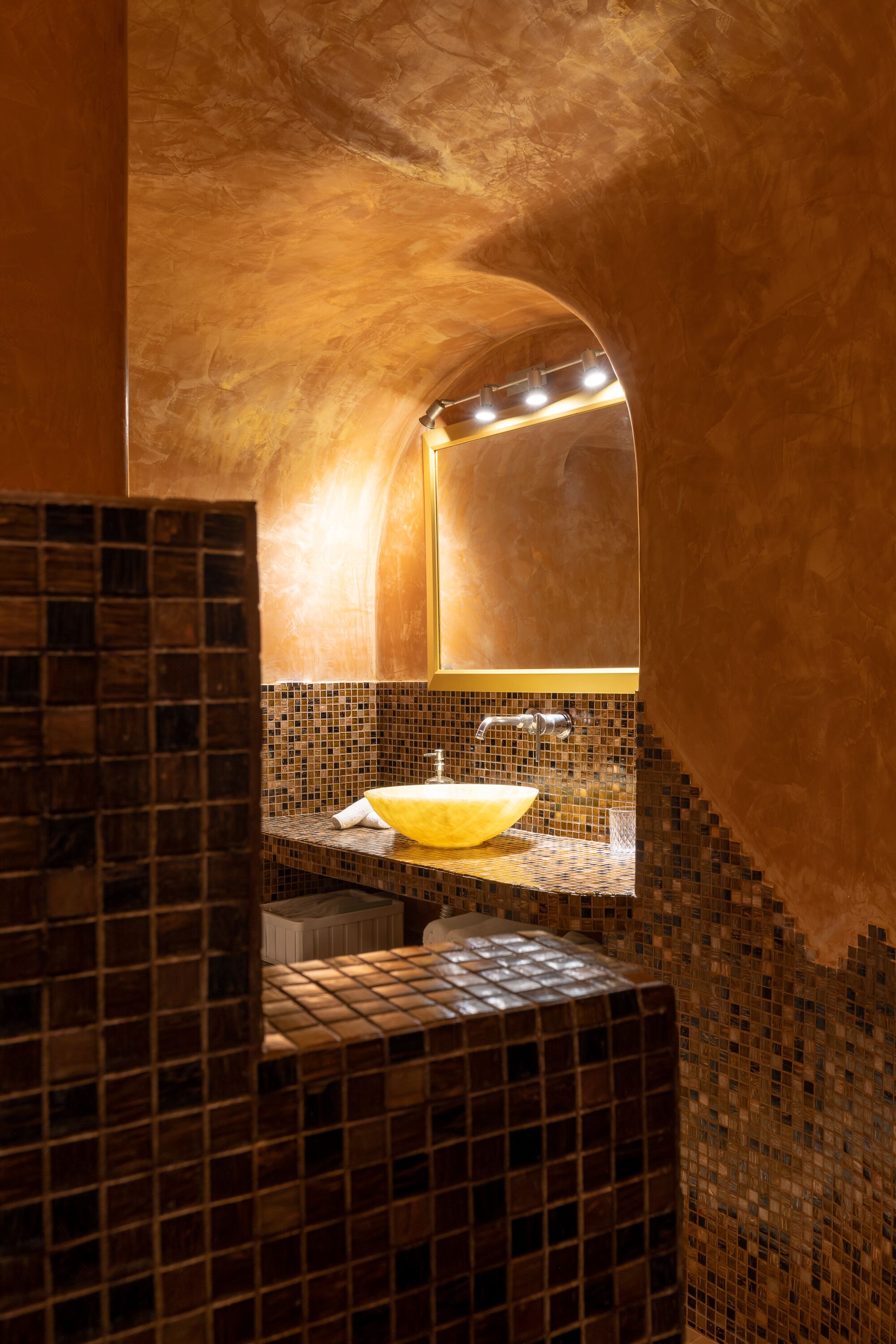 A bathroom with a yellow sink, mosaic tiles, and a curved ceiling.