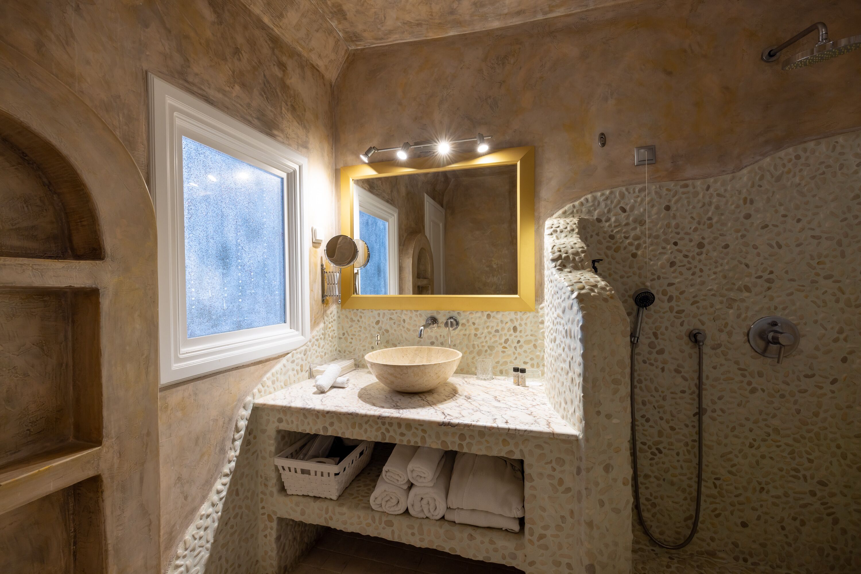 A bathroom with a stone wall, a large mirror, a sink, and a shower.
