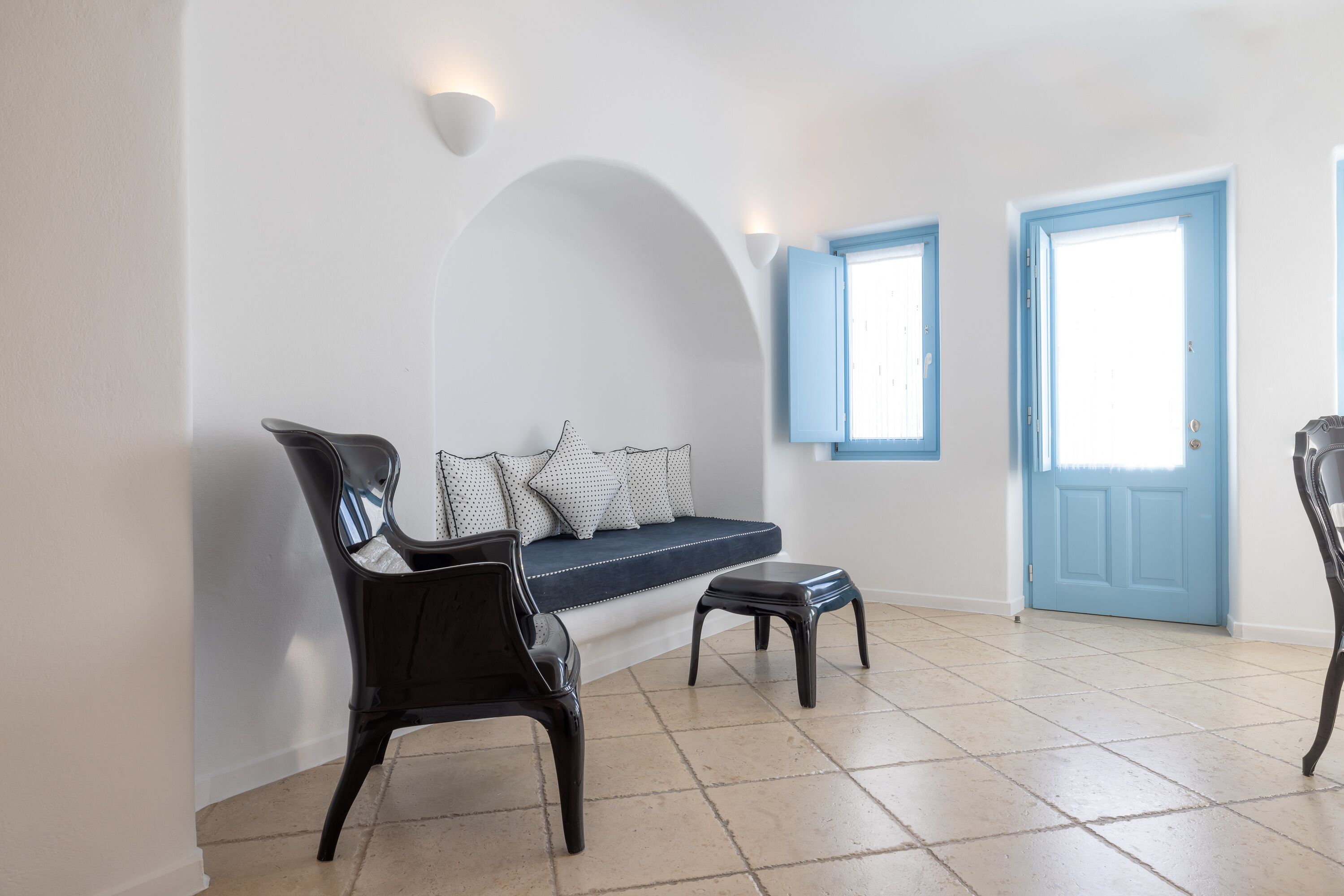 Een kamer met een blauwe deur, een witte muur, een blauwe bank en een zwarte stoel.