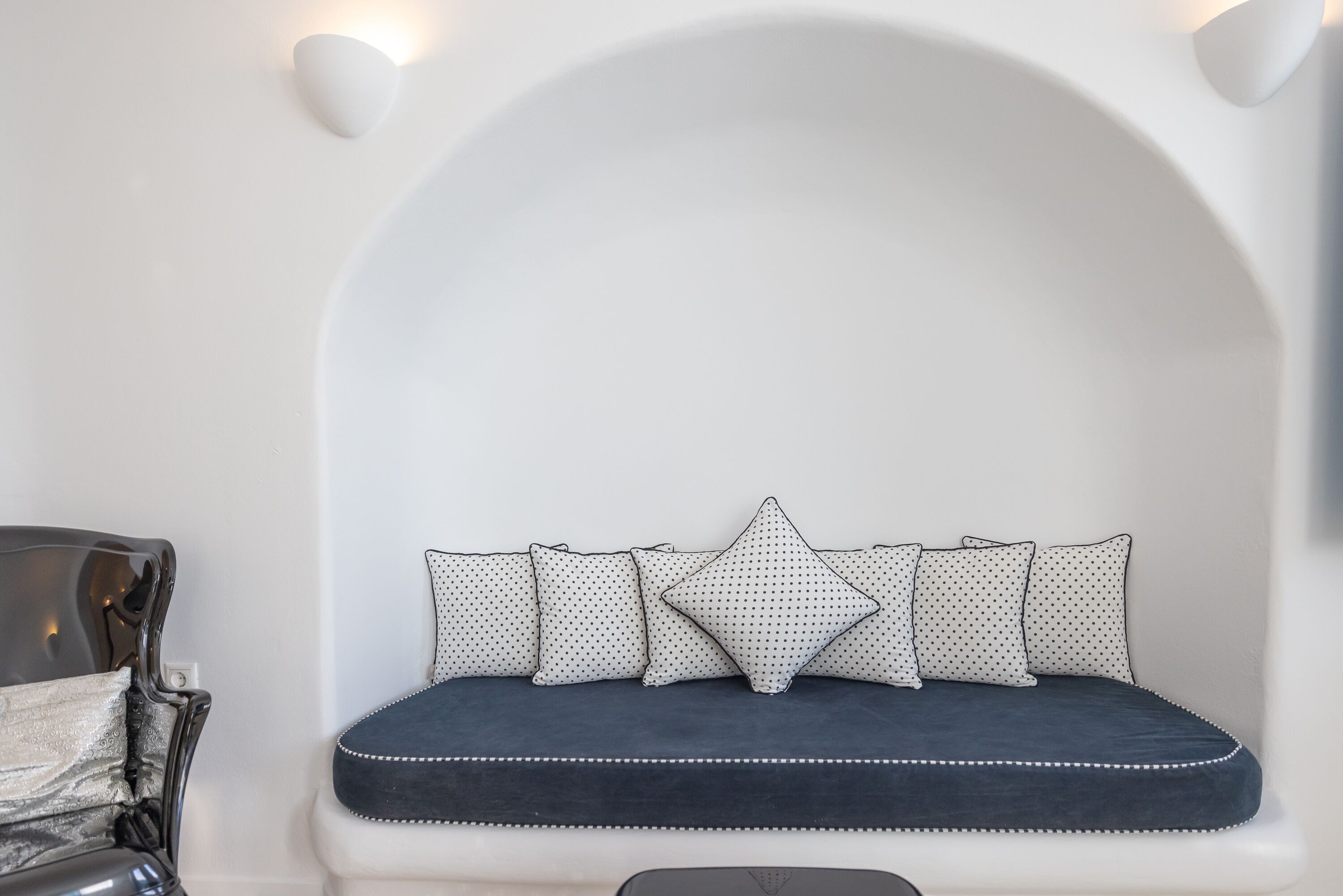 A seating area with a dark blue cushioned bench, white wall, and a single chair with a metallic finish.