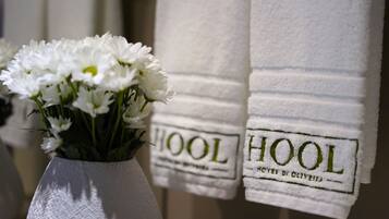 Un jarrón blanco con flores blancas y dos toallas blancas con el bordado 'HOOL'.