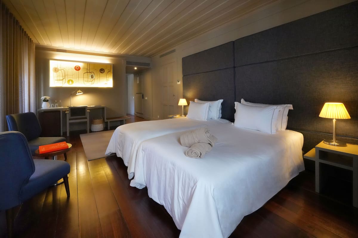 A hotel room with a large bed, two bedside tables with lamps, a desk with a chair, and a wall-mounted artwork.