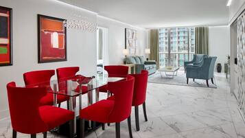 A modern living room with a glass dining table surrounded by red chairs, a sofa, and a blue armchair.